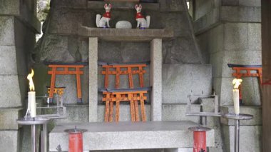 Kyoto, Japonya - 10 Nisan 2025: Her biri geleneksel karakterlerle yazılmış küçük kırmızı torii kapıları ve insanlar mumlarla dolu taş bir anıta dilek tutuyorlar.