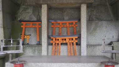 Kyoto, Japonya - 10 Nisan 2025: Her biri geleneksel karakterlerle yazılmış küçük kırmızı torii kapıları ve insanlar mumlarla dolu taş bir anıta dilek tutuyorlar.