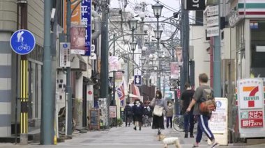 Nara, Japonya - 10 Nisan 2025: İstasyon yakınında çeşitli dükkanları keşfeden yayalarla dolu canlı bir cadde. Sokak tabelaları ve dekorasyonları.