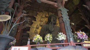 Nara, Japonya - 10 Nisan 2025: Todai-ji Budist tapınağı içinde büyük bir Buda heykeli ziyaretçileri karşılıyor. Heykelin altındaki sunağı renkli çiçekler süslüyor. Büyük Buda Salonunun içi