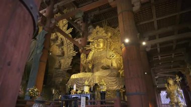 Nara, Japonya - 10 Nisan 2025: Todai-ji Budist tapınağı, karmaşık oymalar ve yumuşak ışıklandırmalarla çevrili muhteşem bir altın Buda heykeline sahiptir. Büyük Buda Salonunun içi