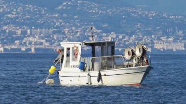 Antibes, Fransa - 2 Mayıs 2025: Beyaz bir kayıkla mavi suya balıkçı ağı atan bir adam görüntüsü