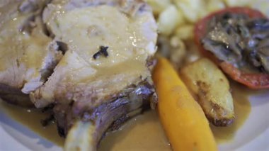 Birkaç parça domuz eti, pişmiş havuç ve domatesin yanında beyaz bir tabağa doldurulmuş yumurta eriştesi yakın.