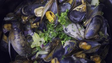 Üstünde yeşil soğan olan bir tencerede çoklu buharlı midyeleri kapat.