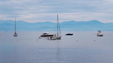 Gündüz vakti arka planda dağlarla denizde çok sayıda tekne hareket ediyor.