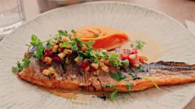 Izgara balığı, patates püresi ve restorandaki bir masada beyaz tabakta sosla kapat.