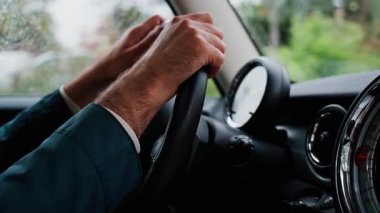 Bir adamın ellerini direksiyona koyup yağmurda yolda araba sürmesi.