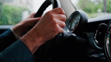 Bir adamın ellerini direksiyona koyup yağmurda yolda araba sürmesi.