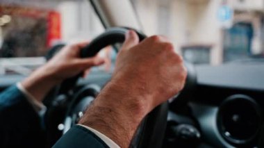 Bir adamın ellerini direksiyona koyup yağmurda yolda araba sürmesi.