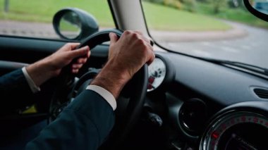 Bir adamın ellerini direksiyona koyup, yolda araba sürerken.