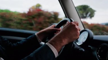 Bir adamın ellerini direksiyona koyup, yolda araba sürerken.