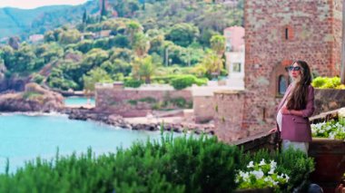 Mandelieu-La Napoule 'daki Chateau de la Napoule Kalesi' nde duran uzun saçlı, güneş gözlüklü hamile bir kadın.