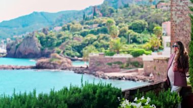 Mandelieu-La Napoule 'daki Chateau de la Napoule Kalesi' nde duran uzun saçlı, güneş gözlüklü hamile bir kadın.