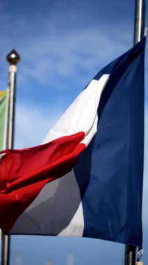 Arka planda mavi bir gökyüzü ile rüzgarda dalgalanan Fransa bayrağının yakınında. Dikey