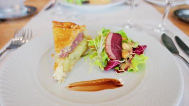 Bir dilim kiş, yanında salata ve restoranda beyaz bir tabakta pişirilmiş et.