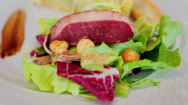 Bir dilim kiş, yanında salata ve restoranda beyaz bir tabakta pişirilmiş et.