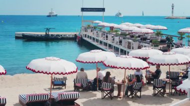 Cannes, Fransa - 13 Mayıs 2025: İnsanlar sahildeki terasta güneş şemsiyeleri altında dinleniyor