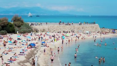 Antibes, Fransa - 17 Mayıs 2025: Arka planda Jaume Plensa 'nın Göçebe şehir heykeli ile Gravette plajında dinlenen insanların yüksek açılı görüntüsü