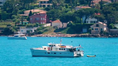 Antibes, Fransa - 24 Mayıs 2025: Akdeniz 'de arka planda yeşilliklerle çevrili villalarla yüzen tekne