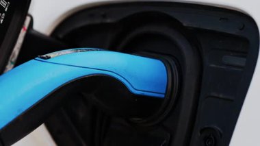 Beyaz bir arabaya takılı mavi bir elektrikli araba şarj aletini kapat.