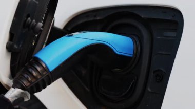 Beyaz bir arabaya takılı mavi bir elektrikli araba şarj aletini kapat.