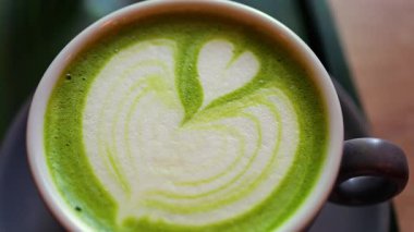 Bir kafede küçük yeşil bir tepside bir kibrit sütlü kahve yakın.