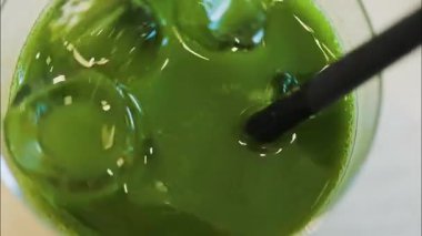 Bir kafede buzlu bir kibriti siyah bir pipetle karıştıran bir elin yakın çekimi.