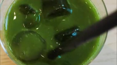 Bir kafede buzlu bir kibriti siyah bir pipetle karıştıran bir elin yakın çekimi.