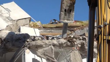 Gündüz vakti hidrolik kırıcıyla beton binayı yıkan bir kazıcı.