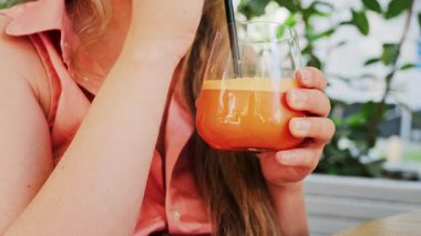 Siyah pipetle bir bardak portakal suyu içen bir kadının yakın çekimi.