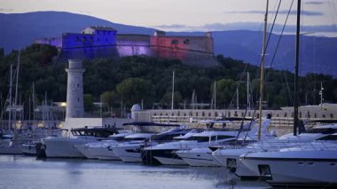 Antibes, Fransa - 8 Haziran 2025: Gemiler Vauban Limanı 'na yanaştı ve Carre Kalesi akşam saatlerinde arka planda aydınlandı