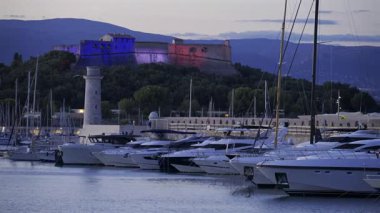 Antibes, Fransa - 8 Haziran 2025: Gemiler Vauban Limanı 'na yanaştı ve Carre Kalesi akşam saatlerinde arka planda aydınlandı