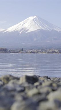 Gün ışığında kayalık ön planda Kawaguchi Gölü 'ne yansıyan karla kaplı dağların büyüleyici manzarası