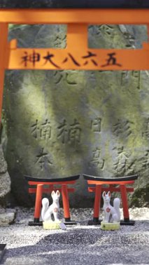 Kyoto, Japonya - 9 Nisan 2025: Antik tapınakta taşın üzerinde duran canlı küçük kırmızı torii kapıları. Fushimi Inari
