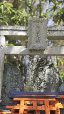 Kyoto, Japonya - 10 Nisan 2025: Taştan kemerleri ve canlı kırmızı torii kapılarıyla Fushimi Inari 'de bir türbe görkemli bir şekilde duruyor. Torii kapılarında Japonca insanlar ve okul isimleri yazılı..