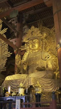 Nara, Japonya - 10 Nisan 2025: Todai-ji Budist tapınağı, karmaşık oymalar ve yumuşak ışıklandırmalarla çevrili muhteşem bir altın Buda heykeline sahiptir. Büyük Buda Salonunun içi