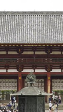 Nara, Japonya - 10 Nisan 2025: Japonya 'daki Todai-ji tarihi tapınağında toplanan kalabalık, serin bir açık hava ortamında baş döndürücü kiraz çiçekleri ve geleneksel mimarinin keyfini çıkarıyorlar..