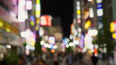 Shinjuku şehrinin hayat dolu manzarası bulanık. İnsanlar akşamları yanan binalarla sokaklarda dolaşıyorlar.