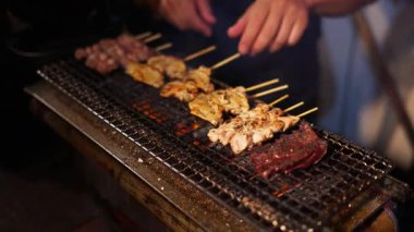 Japon restoranındaki ızgarada Yakitori şişleri pişiren şefin yakın çekimi.