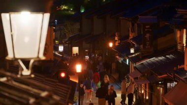 Kyoto, Japonya - 11 Nisan 2025: Ninenzaka taş kaldırımlı yaya yolunda yürüyen ve akşamları geleneksel bina ve dükkanlarla dolu olan bir sokak lambasını kapatın