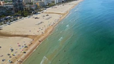 İspanya 'nın Benidorm plajında gün ışığında dinlenen insanların bulunduğu kıyı şeridi boyunca binaların insansız hava aracı görüntüsü.