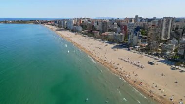 İspanya 'nın Benidorm plajında gün ışığında dinlenen insanların bulunduğu kıyı şeridi boyunca binaların insansız hava aracı görüntüsü.