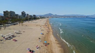 İspanya 'nın Benidorm plajında gün ışığında dinlenen insanların bulunduğu kıyı şeridi boyunca binaların insansız hava aracı görüntüsü.