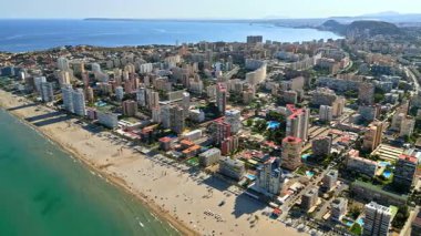 İspanya 'nın Alicante kentindeki plajda gün ışığında dinlenen insanların bulunduğu kıyı şeridi boyunca binaların insansız hava aracı görüntüsü.