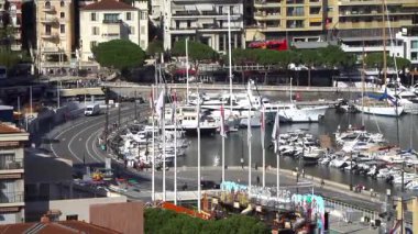 La Condamine, Monaco - 4 Temmuz 2025: Trafikli Quai Albert-1er kavşağı, Monako bayrakları, mevsimlik eğlence ve yerleşim yerlerinin altındaki Herkül Limanı 'na demirlemiş yatlar