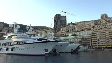 Monte Carlo, Monaco - 4 Temmuz 2025: Rıhtım boyunca lüks konutları bulunan modern katlı Yat Kulübü binasının yakınına kurulmuş yatlar ve lansmanlar