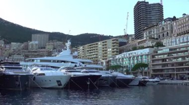 Monte Carlo, Monaco - 4 Temmuz 2025: Rıhtım boyunca lüks konutları bulunan modern katlı Yat Kulübü binasının yakınına kurulmuş yatlar ve lansmanlar