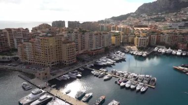 Monaco 'daki Port de Fontvieille' in yüksek açılı manzarası renkli binalar, lüks yatlar ve çevresindeki dağlık manzaraları gösteriyor.