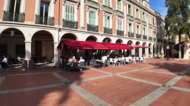 Monako City, Monako - 18 Temmuz 2025: Pastel binalar ve kafe teraslarıyla kaplı geniş bir yaya meydanı, arka planda yükselen dağlar.