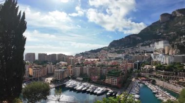 Monaco 'daki Port de Fontvieille' in yüksek açılı manzarası renkli binalar, lüks yatlar ve çevresindeki dağlık manzaraları gösteriyor.